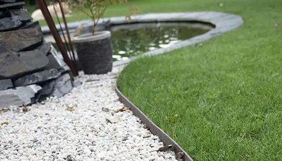 bordure sinueuse qui sépare un parterre de cailloux blanc d'une belle pelouse bien tondue. En arrière-plan, il y a un joli plan d'eau